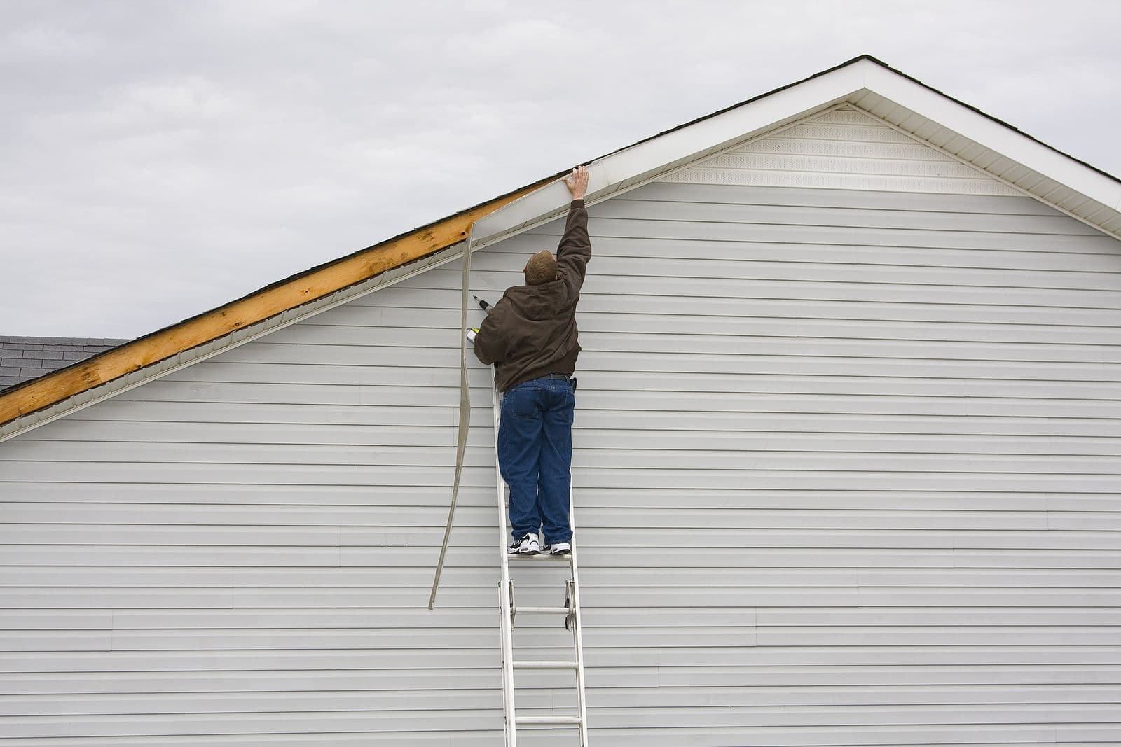 A worker installs light-colored siding.